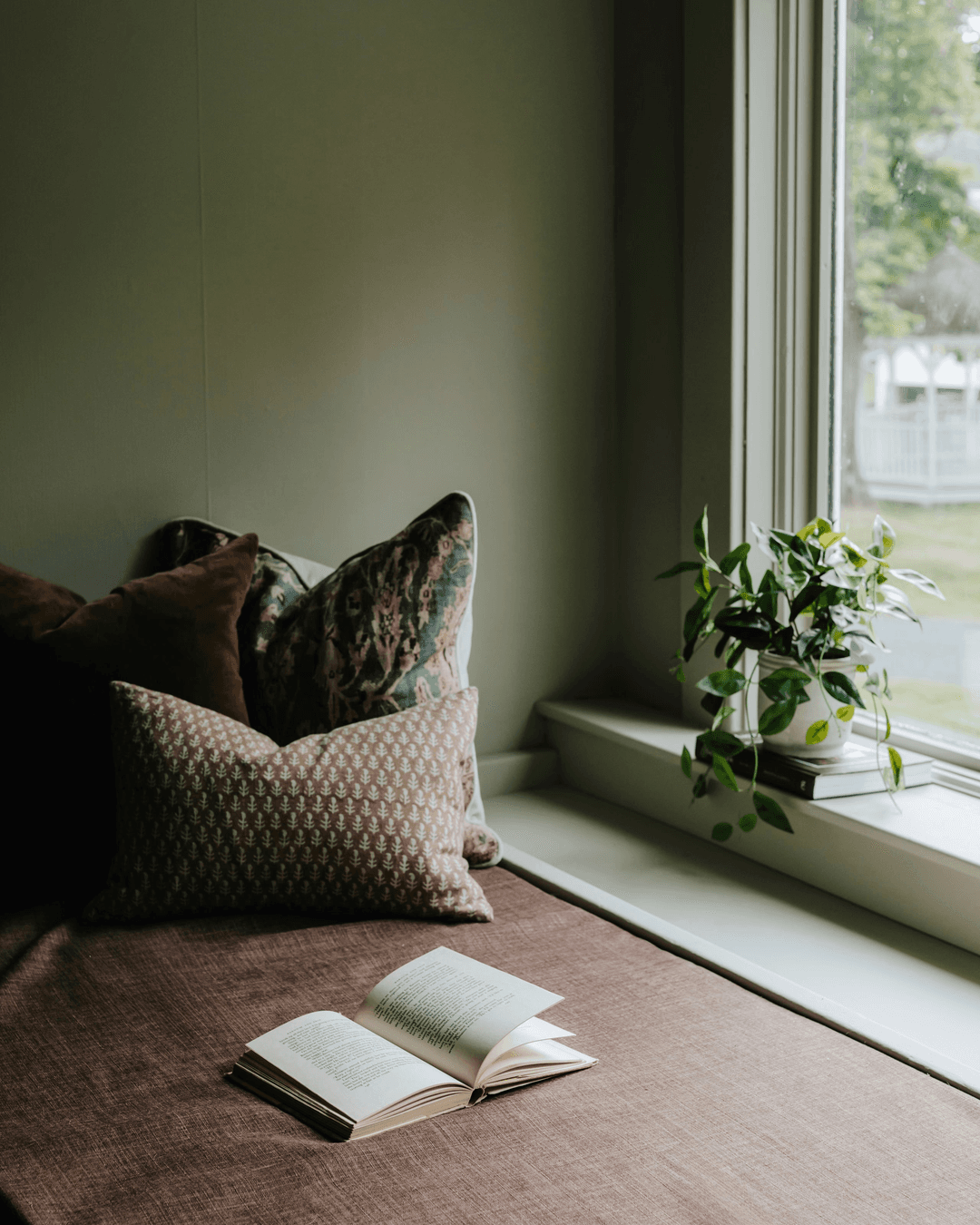 open notebook on a brown desk with throw pillows by the side and green houseplant by the glass window